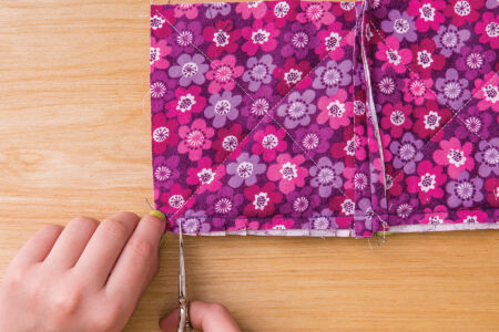 person using scissors to cut along the edge of sewn pink floral fabric